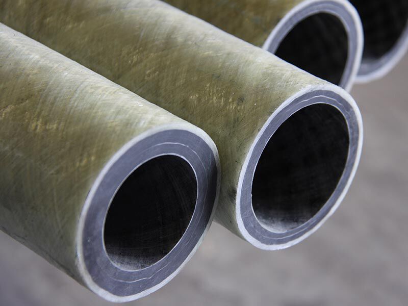 Image shows the end of several tubes suspending over a light grey background. The tube have carbon fiber interior layers and exterior fiberglass layers.